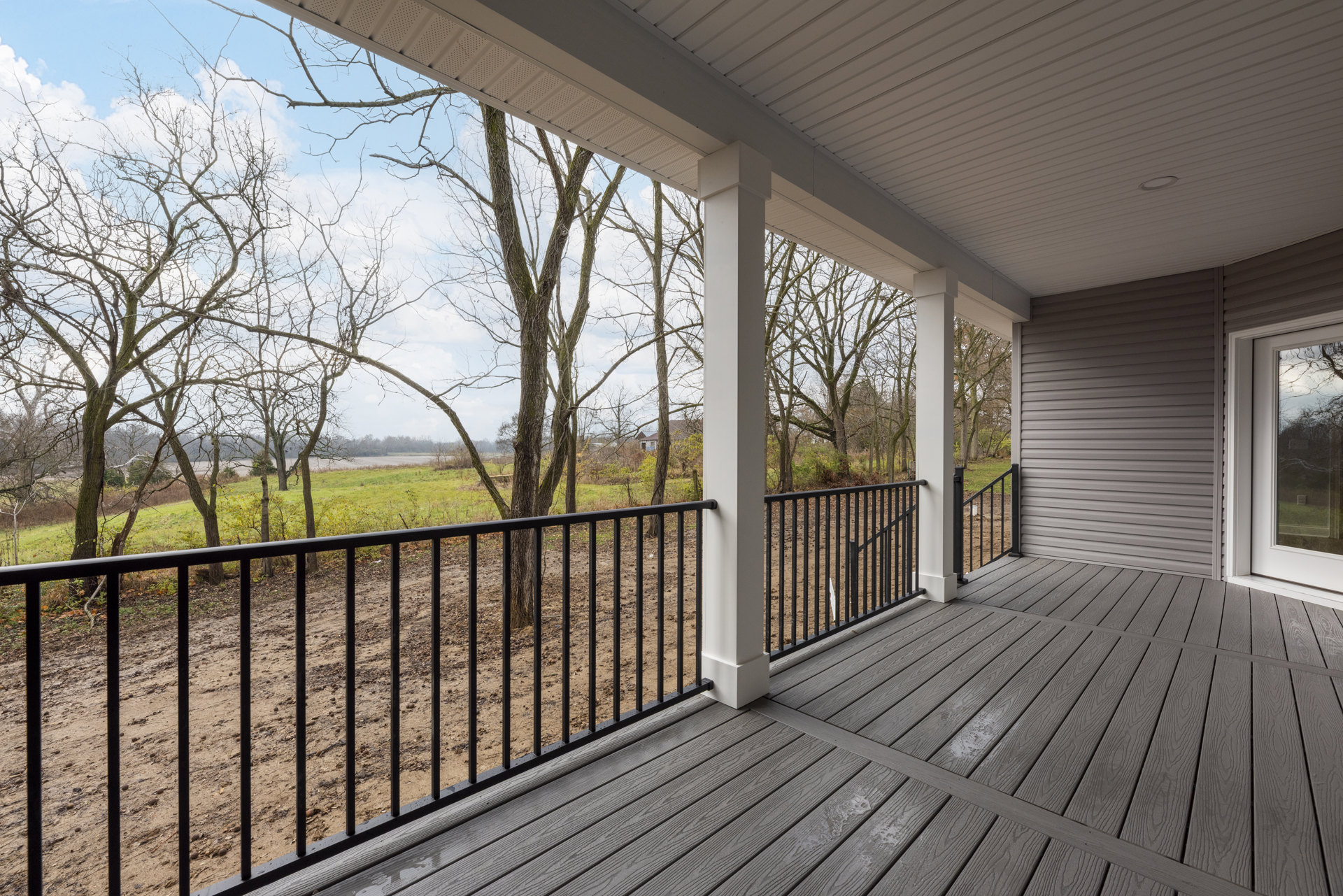 Wood deck with metal railing, surrounded by trees and greenery, white column and roof visible, outdoor residential setting