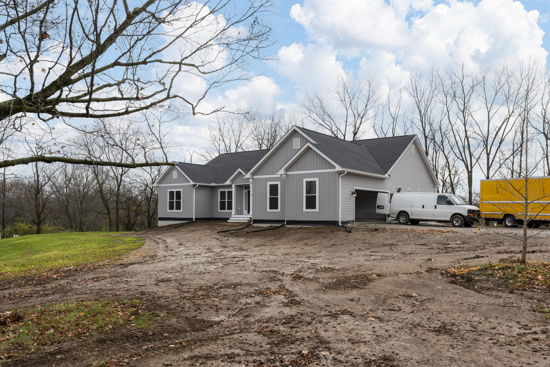 Two-story house with white-framed windows, surrounded by tall trees, yellow truck parked on dirt driveway in front