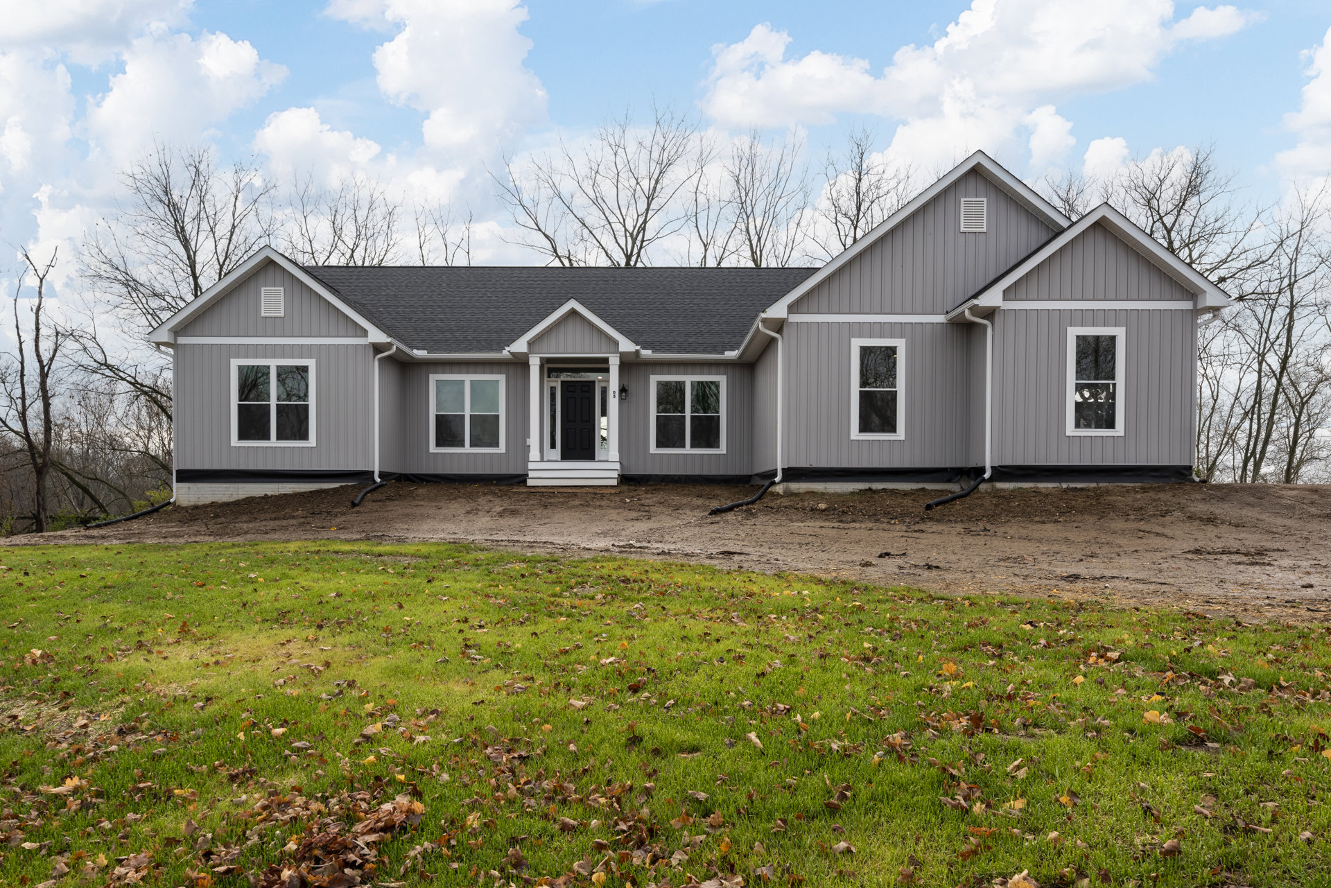 Two-story home with white siding, black front door, multiple windows with white frames, surrounded by green lawn and scattered brown leaves, Robert Frost Farm visible in the