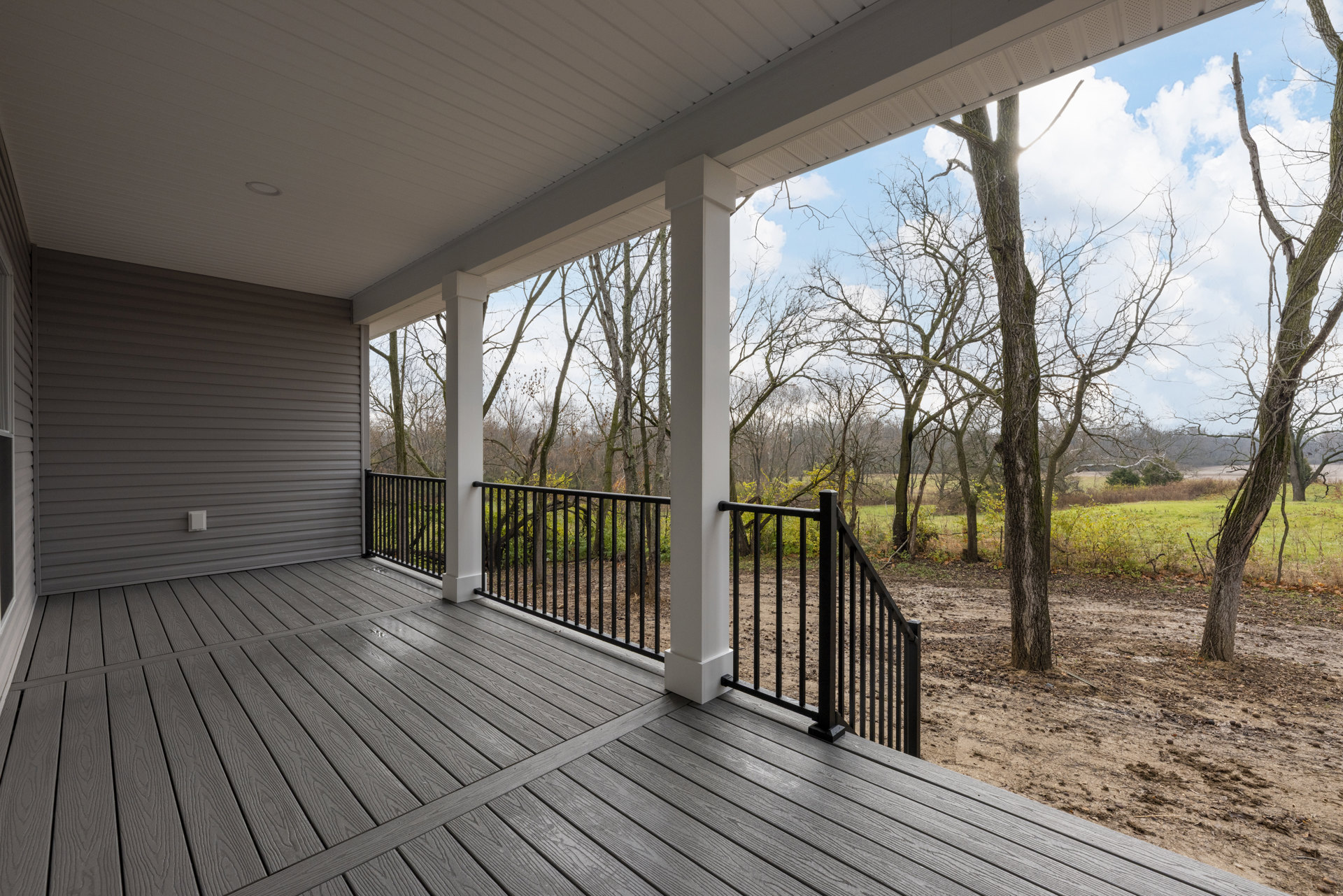 Wood deck with metal railing overlooking leafy trees, tall white pillar visible among branches, outdoor porch area bathed in natural light
