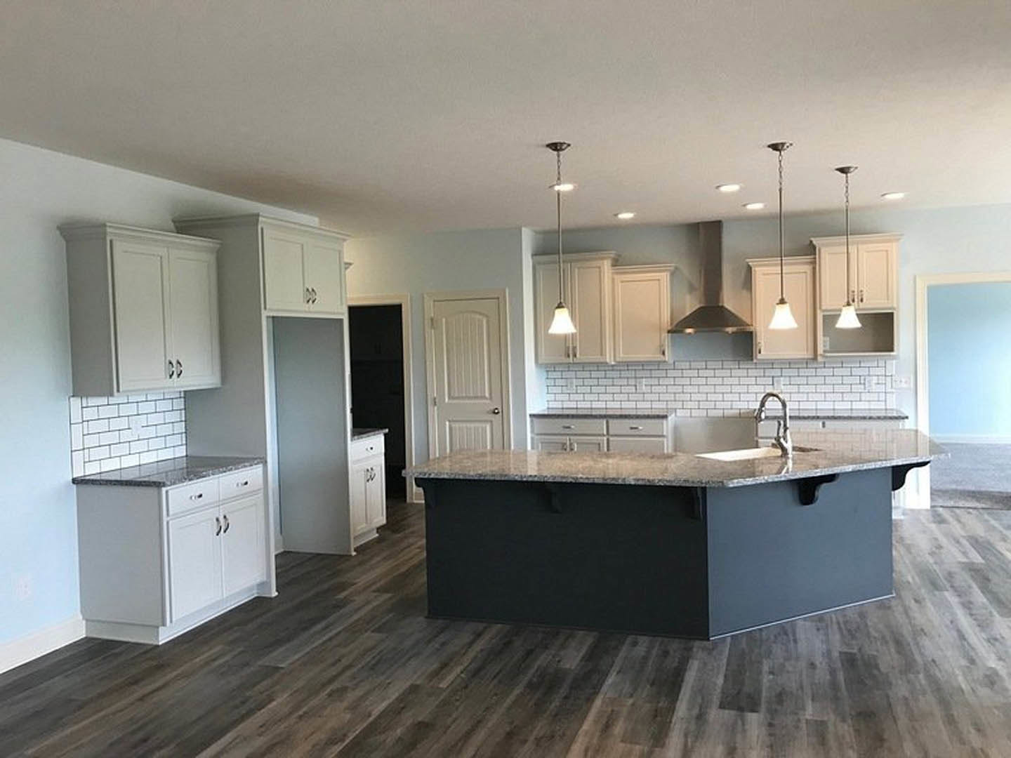 Spacious kitchen featuring a large marble-topped island with built-in sink, white cabinetry with silver handles, tiled flooring, and modern pendant light fixture.