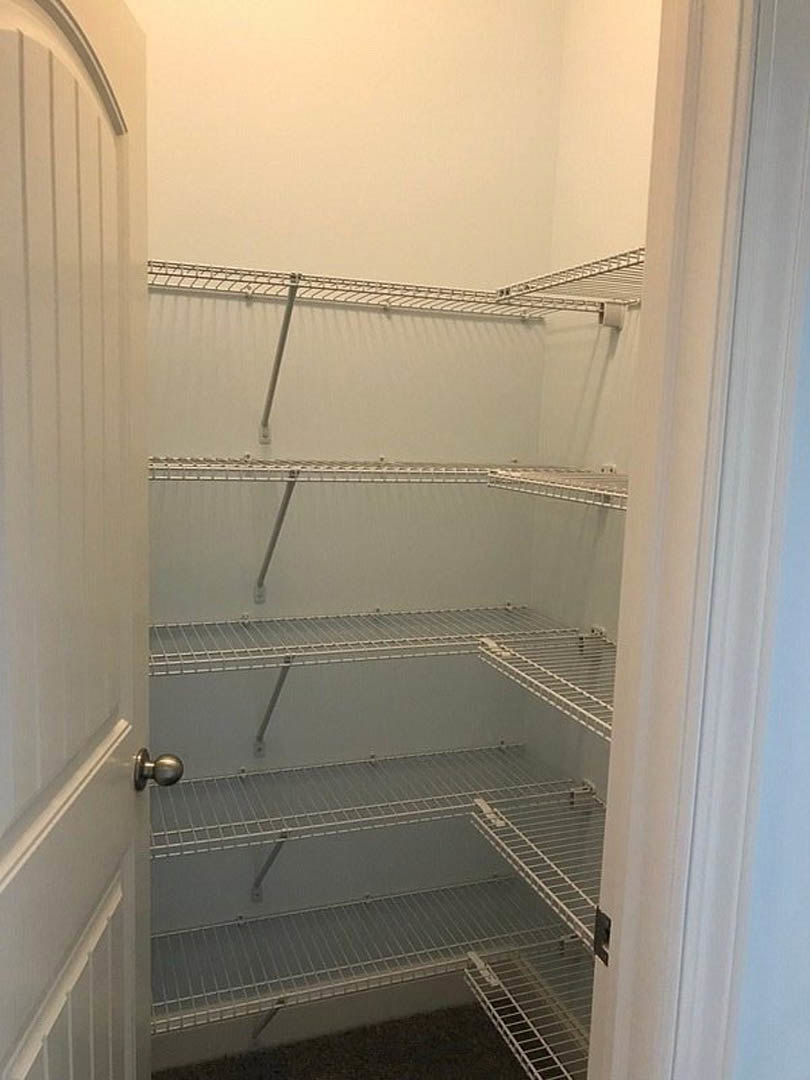 Closet with white plaster walls, built-in metal shelves, black and white door, metal floor grate, and close-up of a round door knob