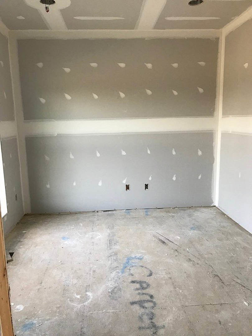 White-painted walls, unfinished concrete floor with handwritten markings, wall with small holes, scattered white paint drops on gray surface.