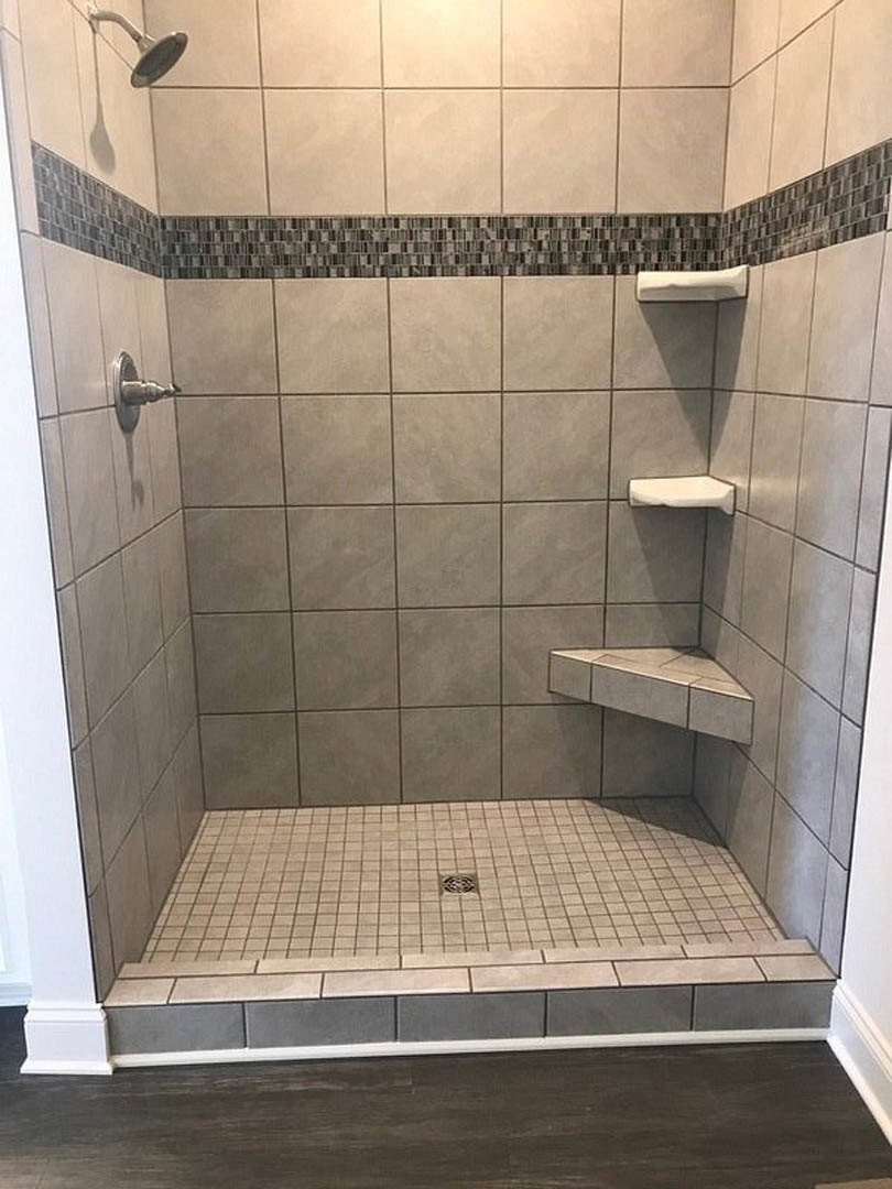 Walk-in shower with light gray tile floor, linear drain, white tiled walls, chrome showerhead, and modern faucet