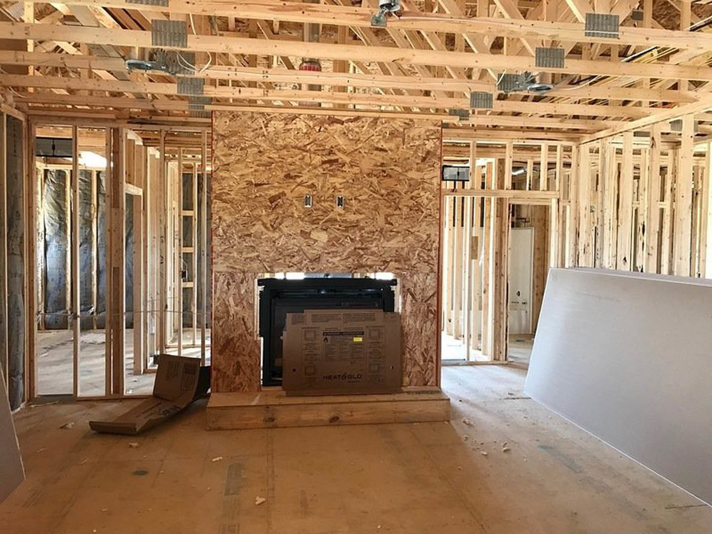 Living room with stone fireplace, mounted television above mantel, hardwood floors, white walls, exposed ceiling beams, and cardboard moving box near doorway.