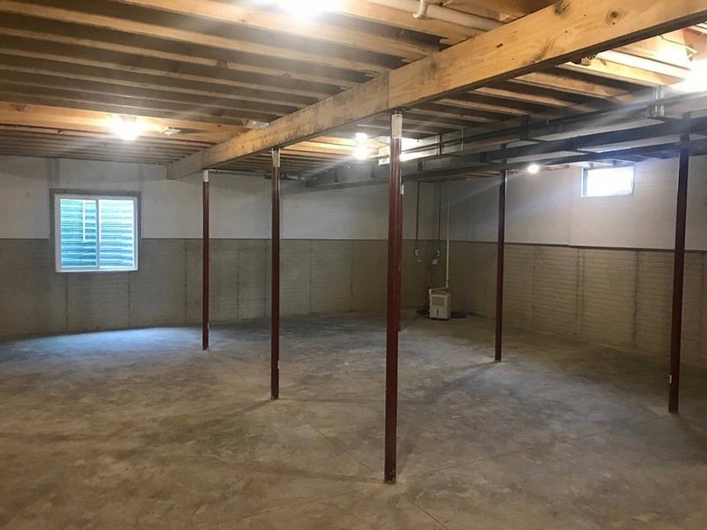 Room with exposed wooden ceiling beams, plaster walls, concrete floor, and a window fitted with blinds.