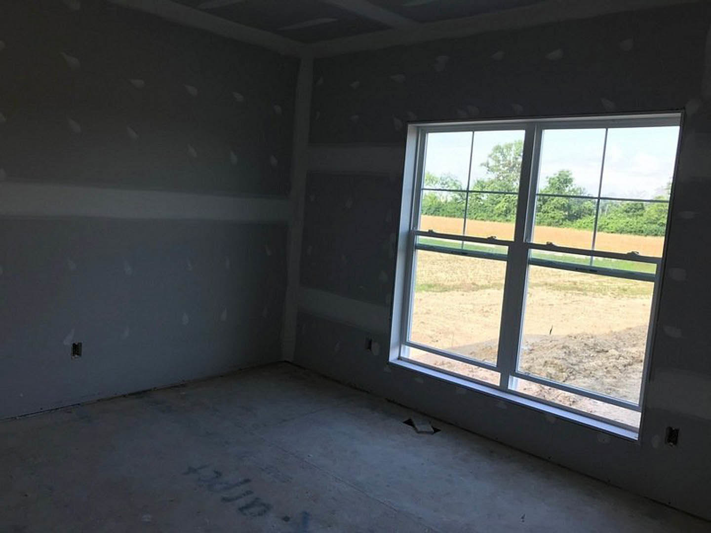 Concrete floor with handwritten markings, black accent wall with white dot pattern, large window overlooking grassy field and trees.