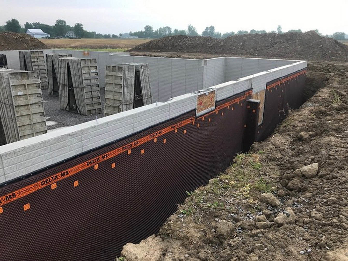 Concrete foundation slab with embedded rebar, surrounded by dirt, rocks, and construction materials, under a clear sky.