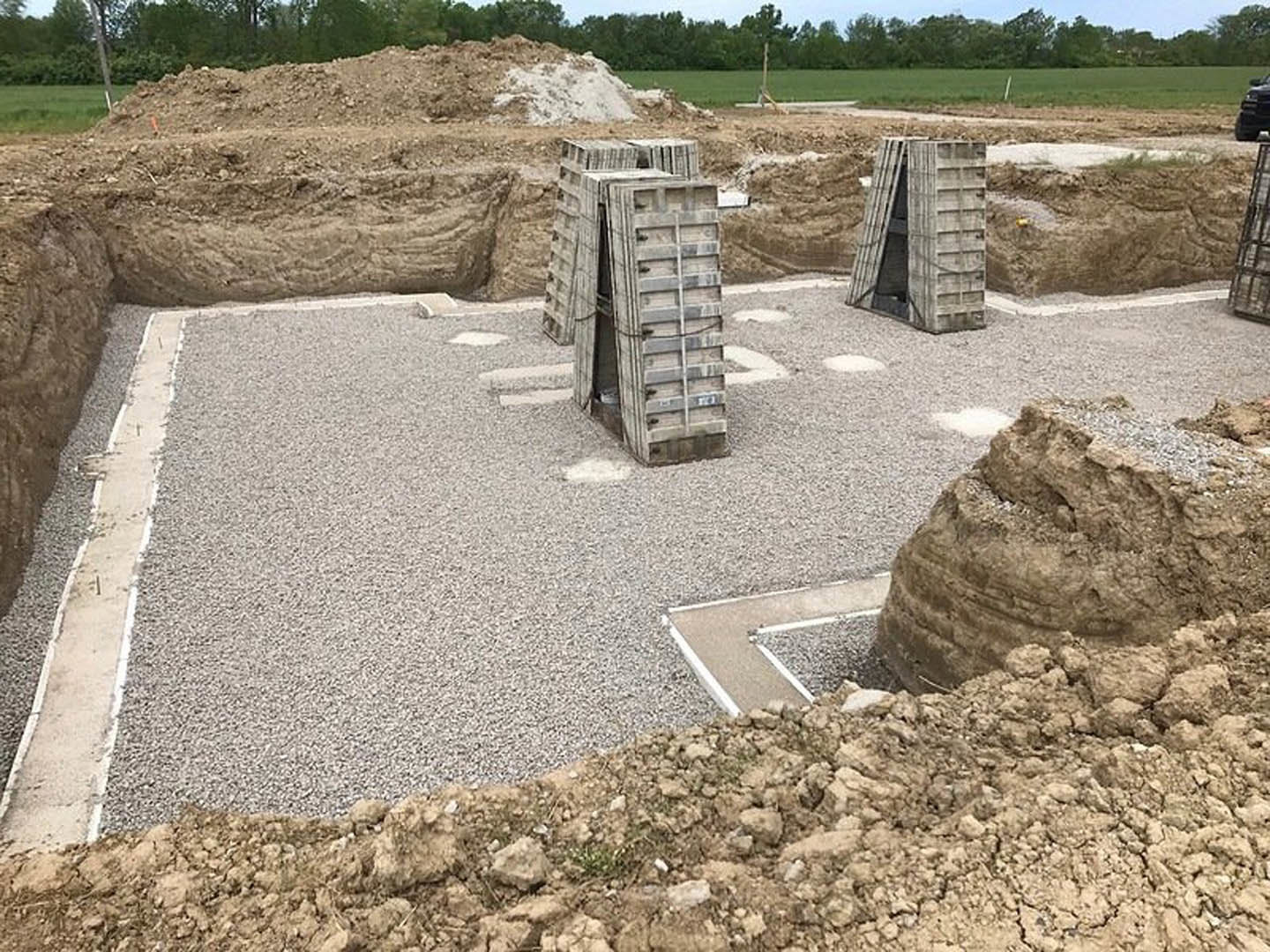 Gravel pile and unfinished wooden framing on a residential construction site, open doorway visible, surrounded by exposed soil and stone.