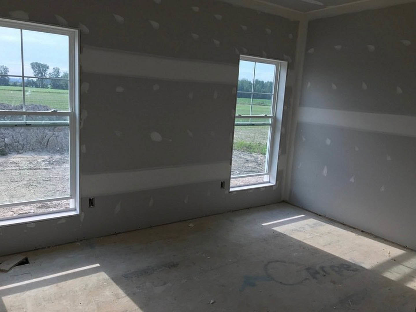 Concrete floor and white walls in a bright room featuring large windows overlooking a grassy field and fence, with a person standing near the wall.