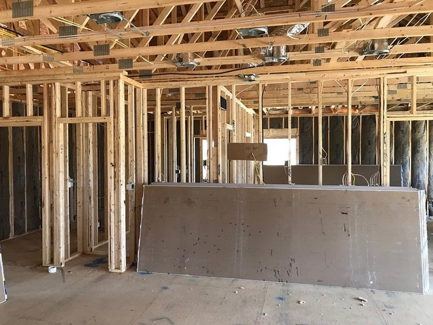 Exposed wooden ceiling beams, unfinished drywall wall, concrete floor, and construction materials in a residential interior under construction