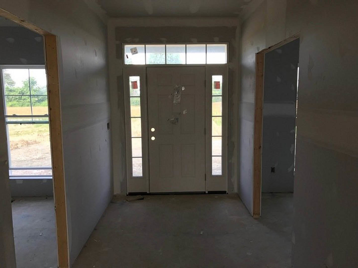 White paneled door with glass inserts, grey wood flooring, white baseboards, adjacent window with wooden frame, two doors visible in bright interior room.