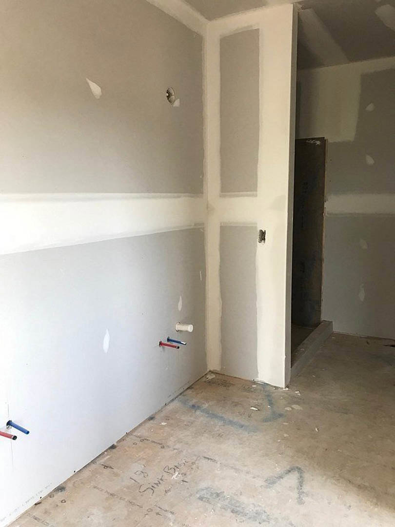 Room with white walls and trim, concrete floor marked with blue lines and writing, black accent wall bordered in white