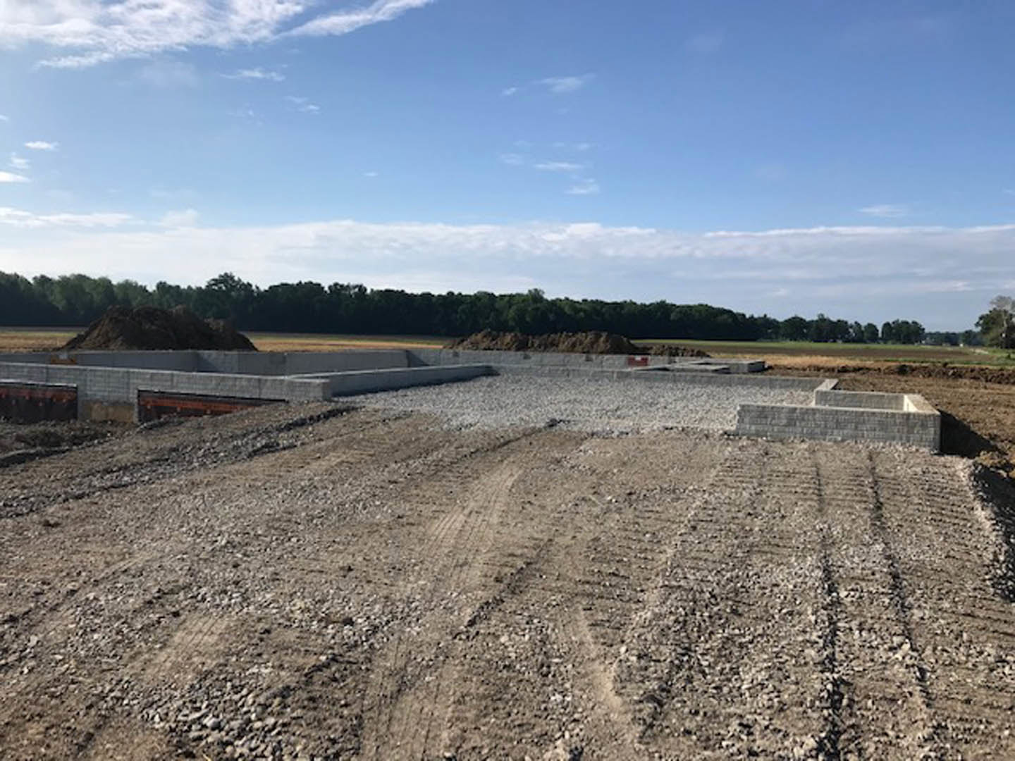 Dirt construction site with tire tracks, scattered trees in the background, blue sky with clouds, black cat lying on the ground