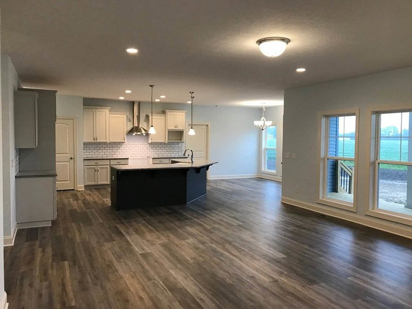 Open kitchen and dining area with wood flooring, black countertop, modern cabinetry, pendant light fixture, large windows offering lake view