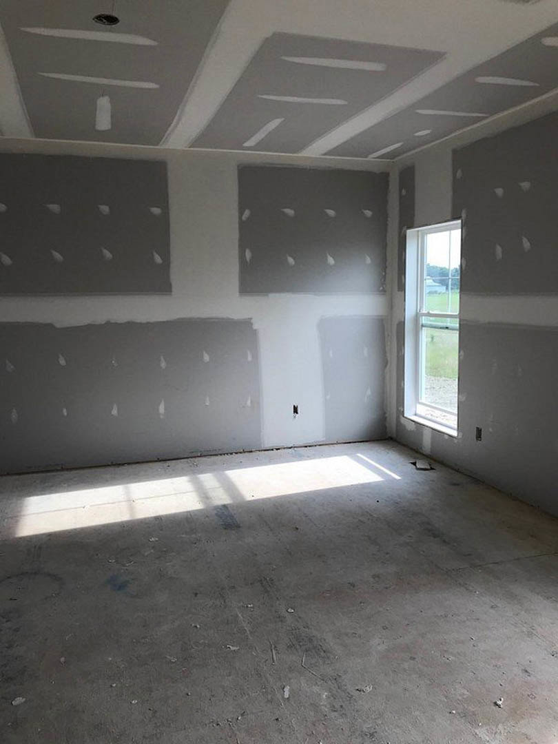 Room with white and gray plaster walls, sunlight streaming through window onto light-colored flooring, green field visible outside, close-up of floor light fixture, wall with white