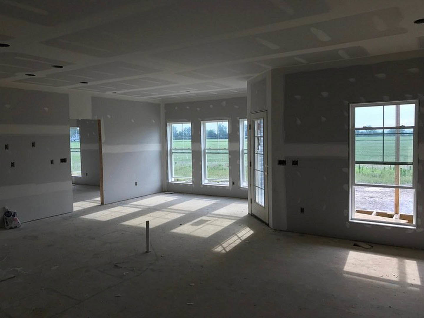 Spacious room featuring large windows with views of an open field, white walls, wood flooring, and a glass door allowing natural daylight.