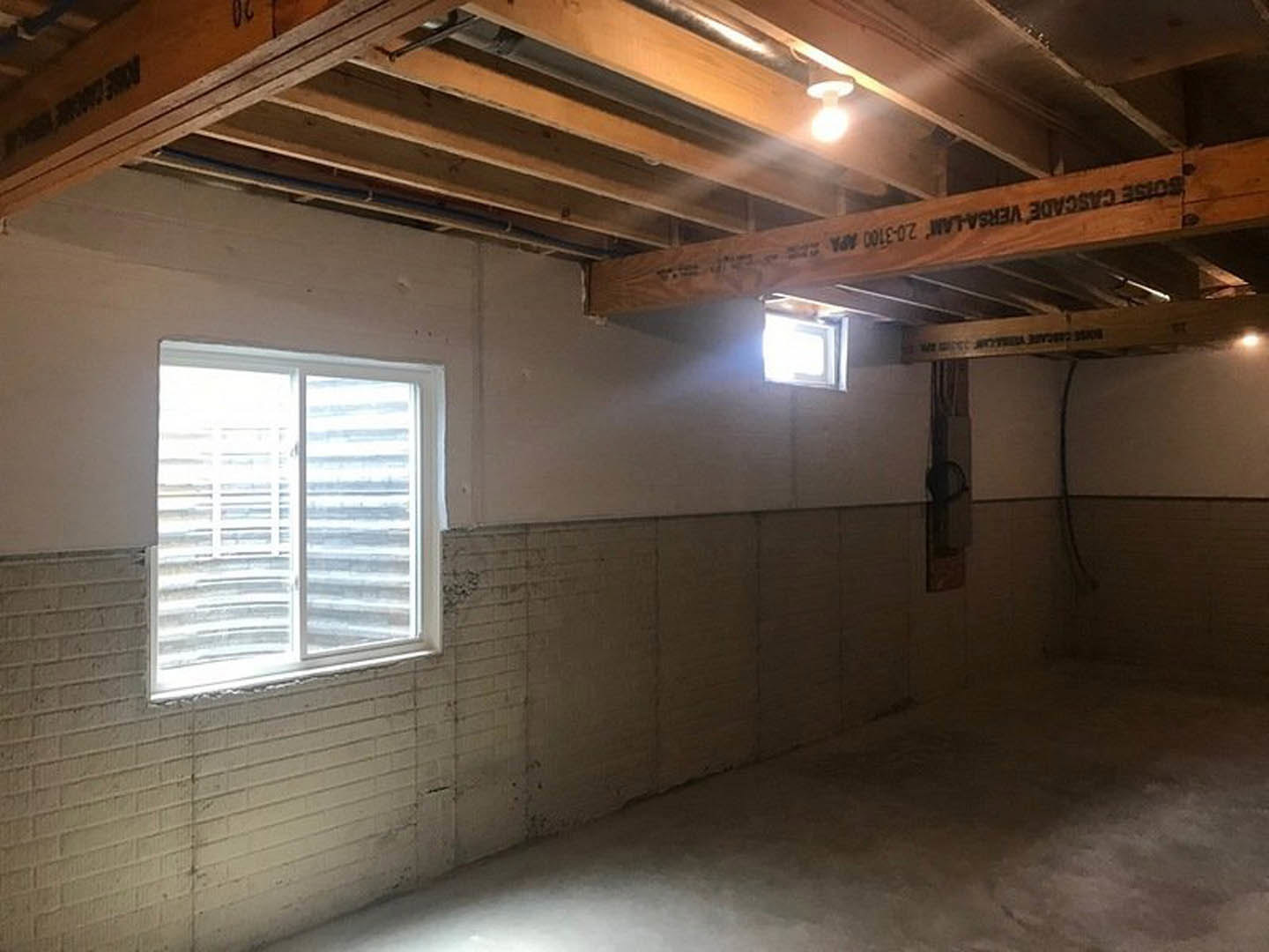 White-framed window set in a brick accent wall, sunlight streaming onto a white plaster floor, exposed ceiling beam with black lettering, minimalist interior with natural daylight.