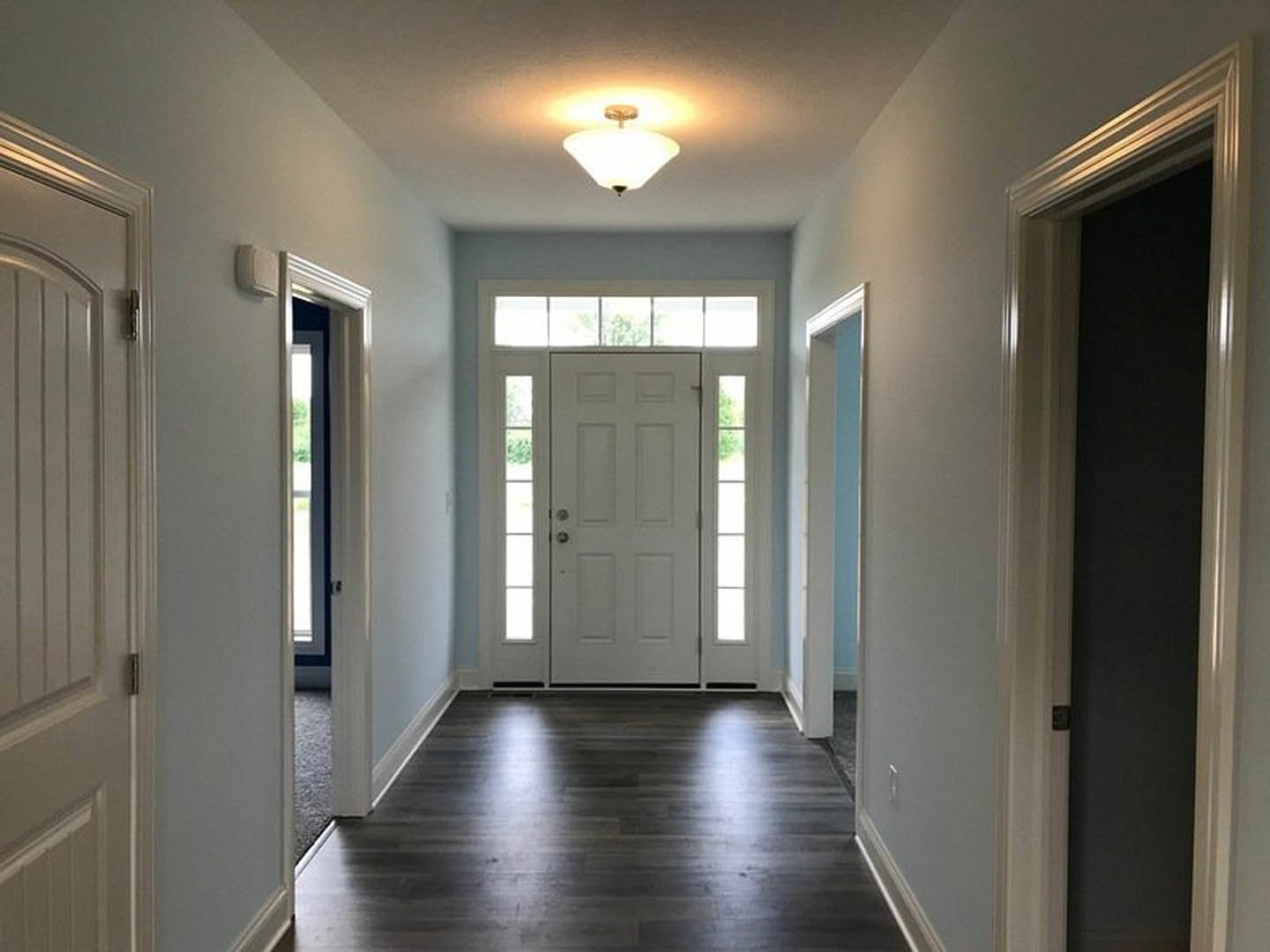 Hallway with dark wood flooring, white door featuring glass panes and silver handle, ceiling light fixture, white walls with molding