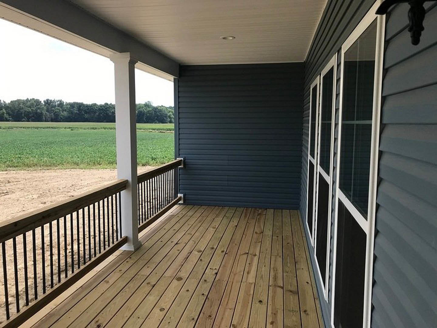 Wooden porch with black siding and white posts, fenced deck overlooking grassy field and distant trees