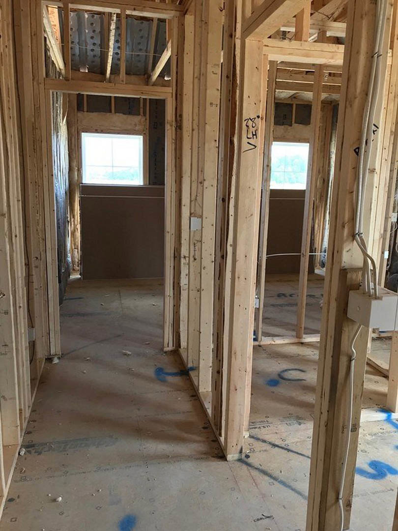 Exposed wood framing and beams inside a house under construction, with visible insulation, white-framed window, and unfinished surfaces.