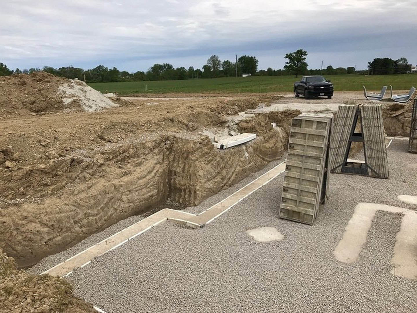 Black pickup truck parked beside a dirt excavation pit, surrounded by rocky soil and sparse trees under a cloudy sky