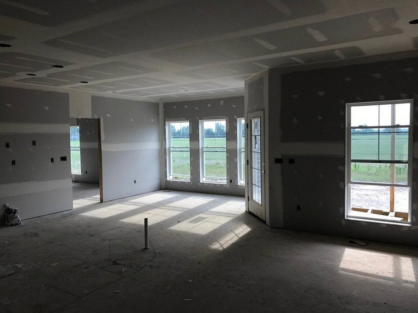 Spacious room featuring large windows overlooking a green field, light-colored walls, hardwood flooring, and ceiling fixtures.