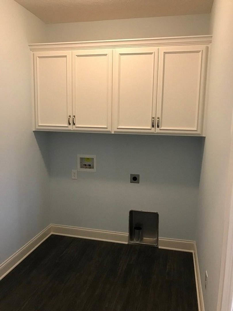 White kitchen cabinets with black wood flooring, white trim, a metal trash can recessed in cabinetry, white walls, and a white door with a black handle.
