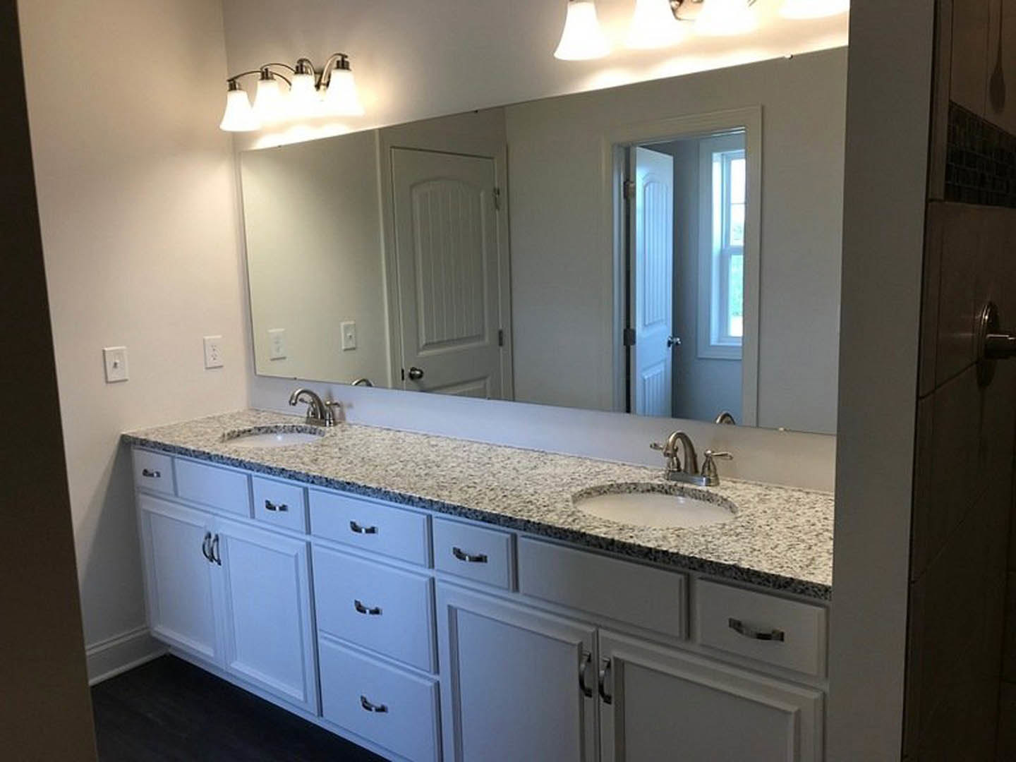 Bathroom with stone tile accent wall, expansive mirror above quartz countertop, modern chrome faucet, and wood cabinetry with sleek drawers.