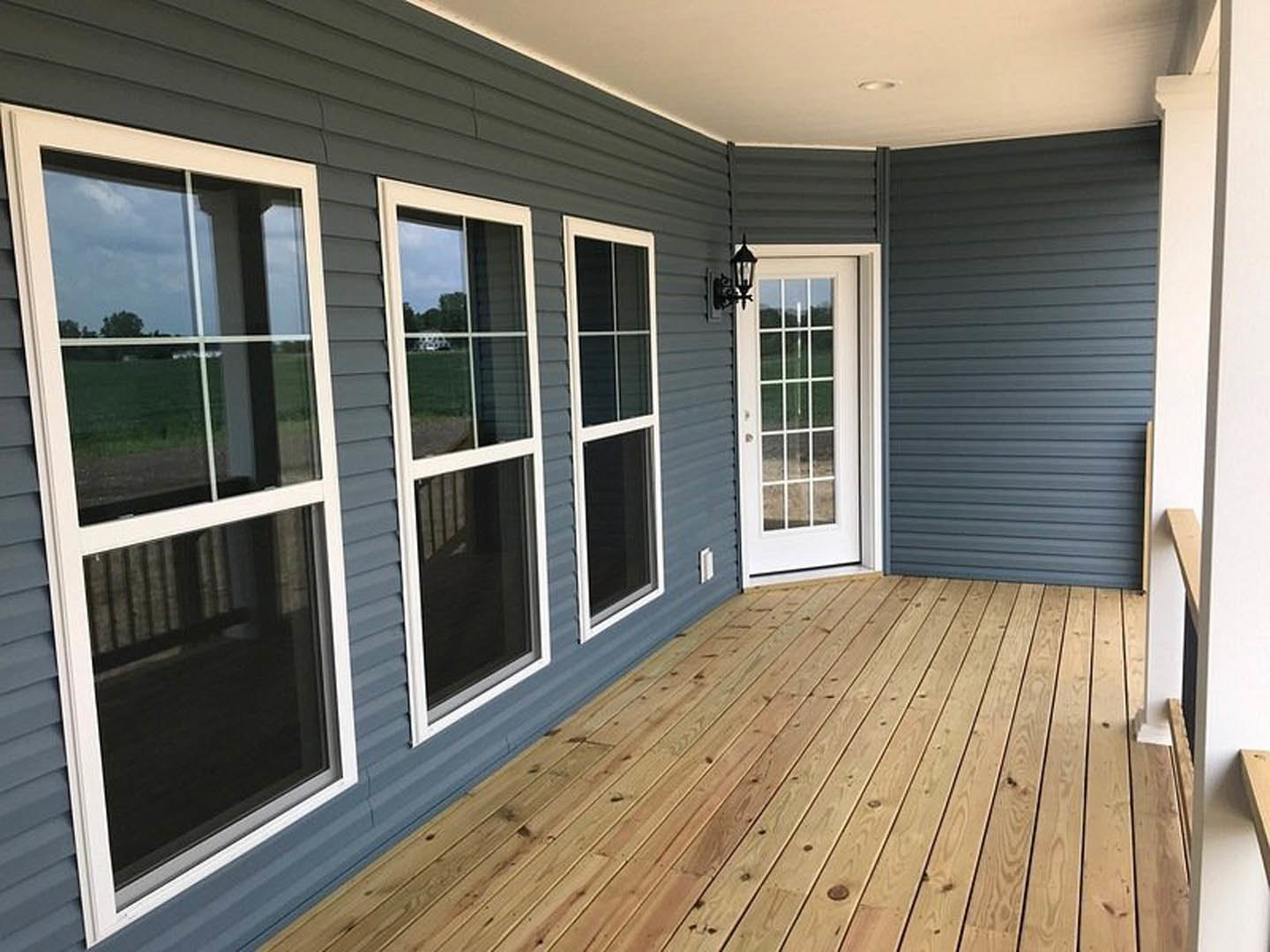 Wooden deck with horizontal planks, glass door, and large windows framed in white on residential home exterior