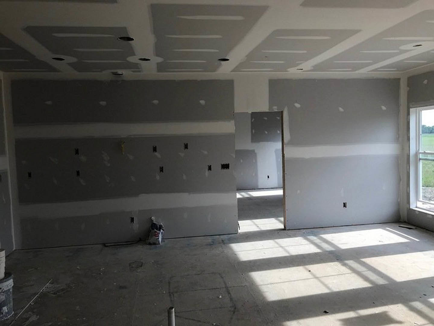 White plaster wall with a wooden door, sunlight casting window shadows across smooth concrete floor, partial view of ceiling and window frame