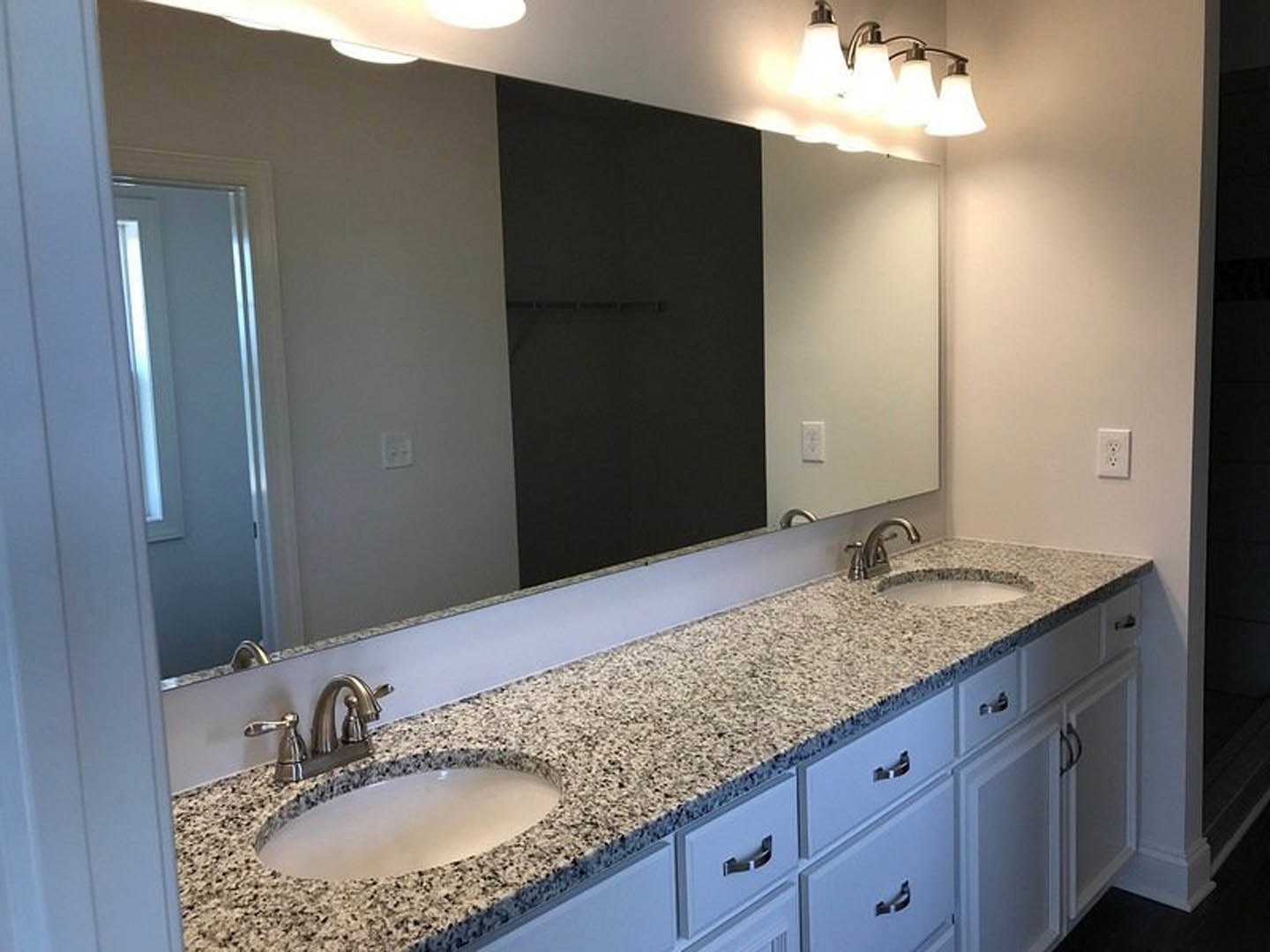 Bathroom with expansive wall mirror, white countertop and undermount sink, chrome faucet, tile backsplash, modern light fixture, and visible electrical outlet.