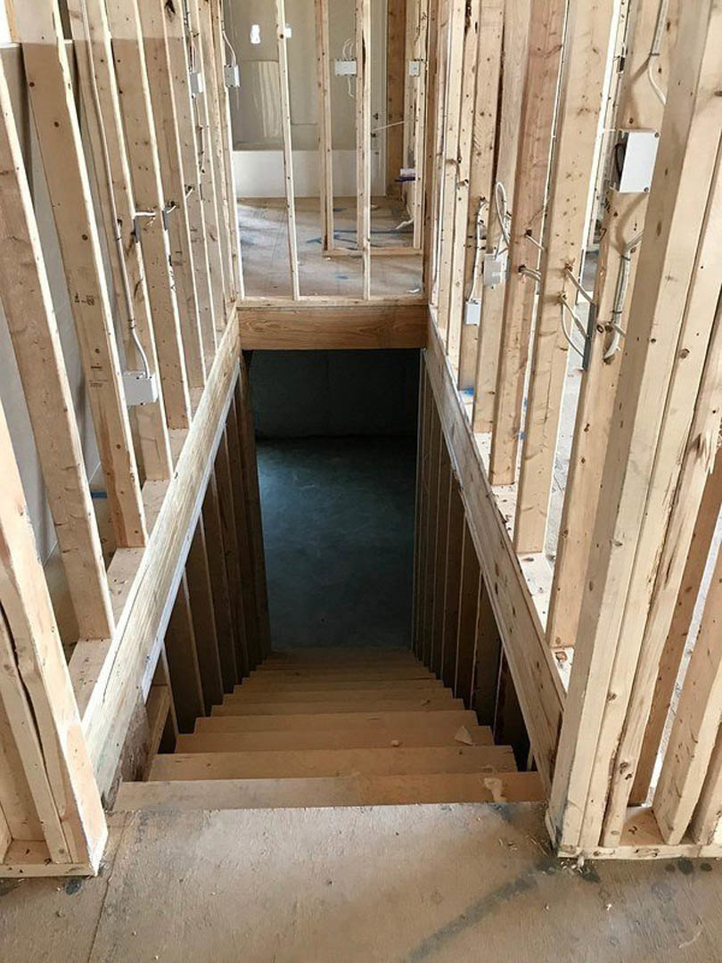 Wood-framed staircase with unfinished lumber steps leading to an upper room, open doorway visible, concrete floor and exposed framing along walls in a house under construction