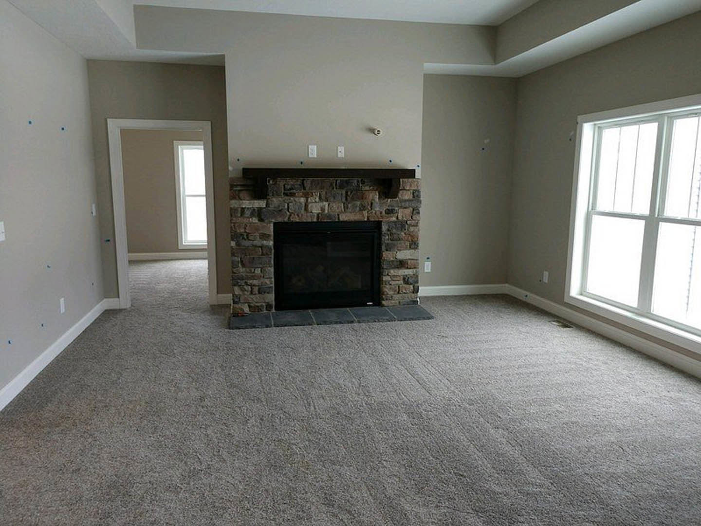 Living room featuring a stone fireplace, carpeted walls, carpeted floor, large window, and wood burning stove