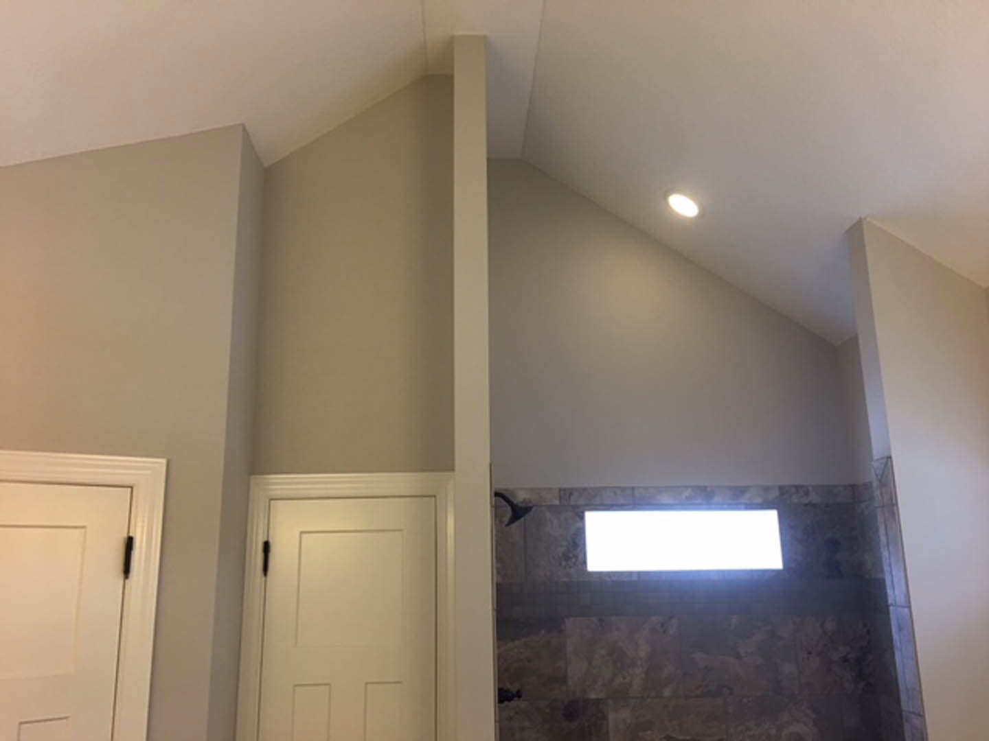Bathroom with gray stone tiled wall, white door featuring black handle, rectangular wall light fixture, and white trim molding