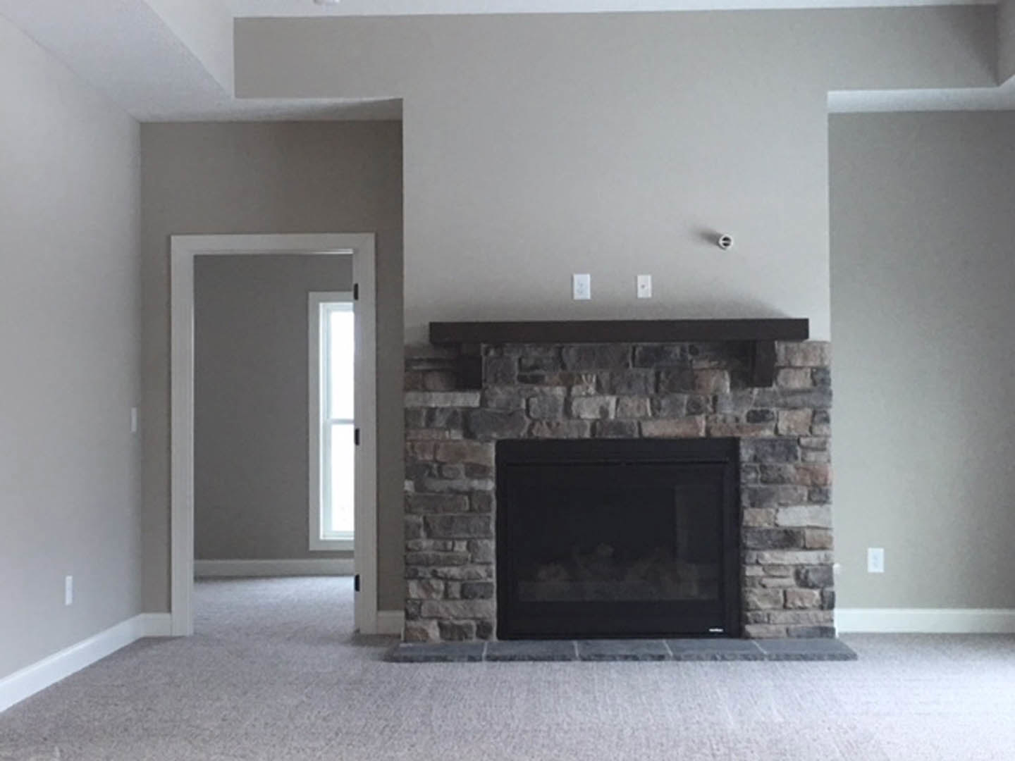 Stone fireplace with black fire screen, wood mantel shelf, and hardwood floors in a living room.
