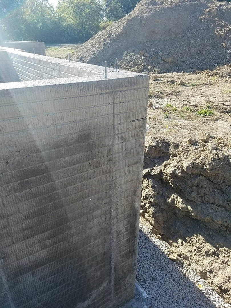 Concrete retaining wall beside a large pile of dirt and rocks, outdoor mountain setting with blurred forest background