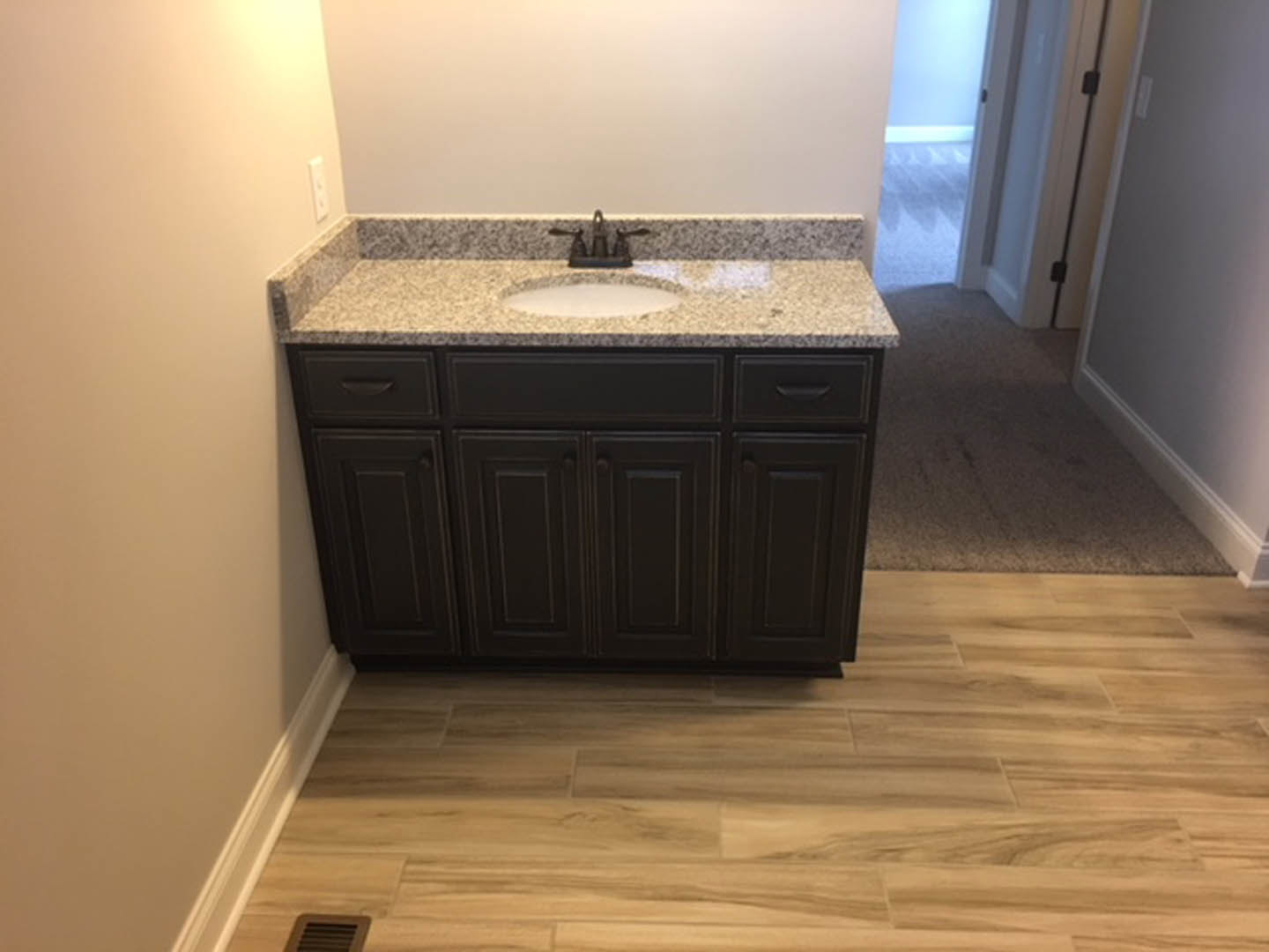 Bathroom with wood flooring, black cabinet, white countertop and sink, wall vent, and tile accents
