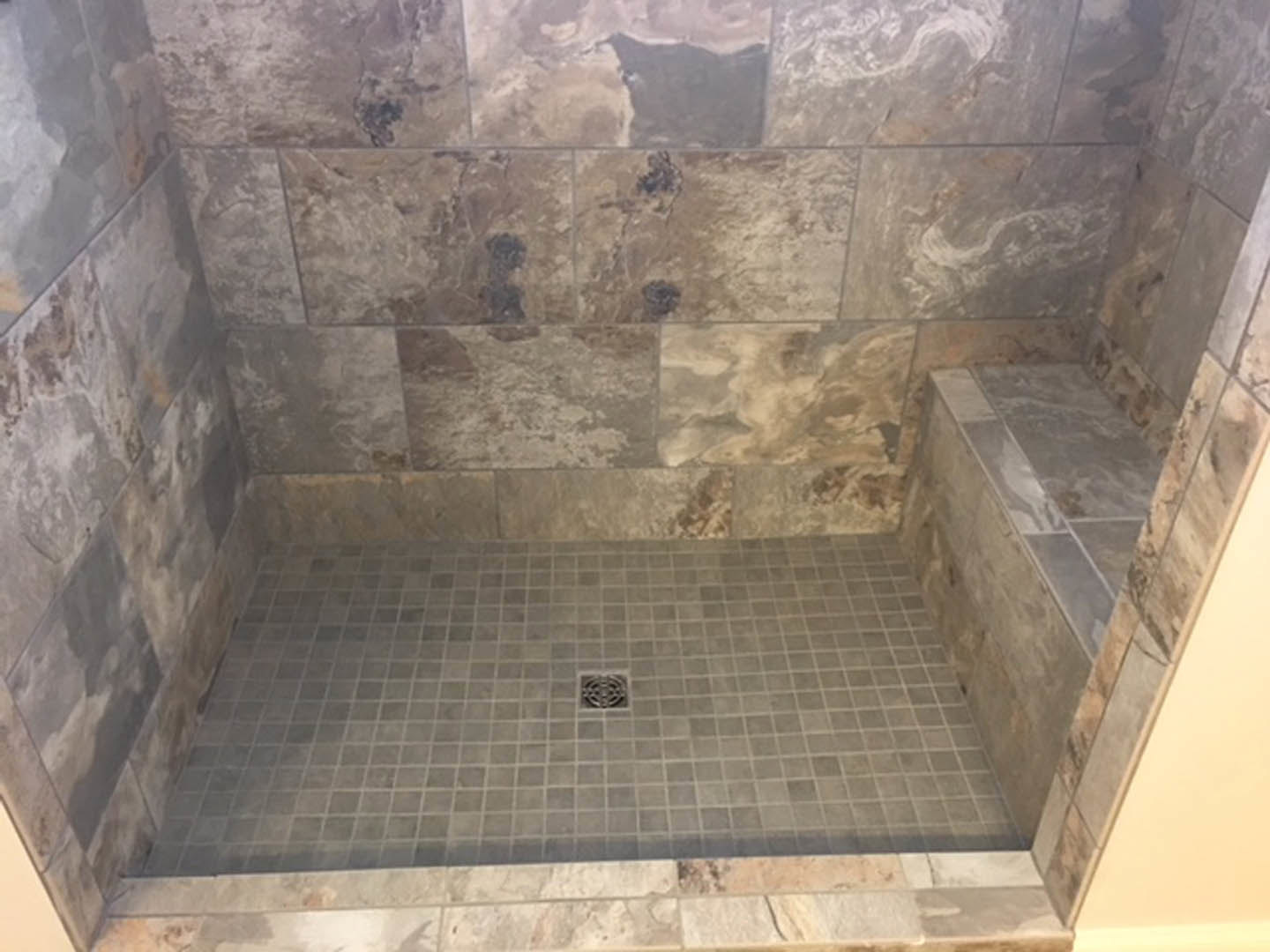 Shower with stone tile floor, square drain, and tiled walls in a modern bathroom