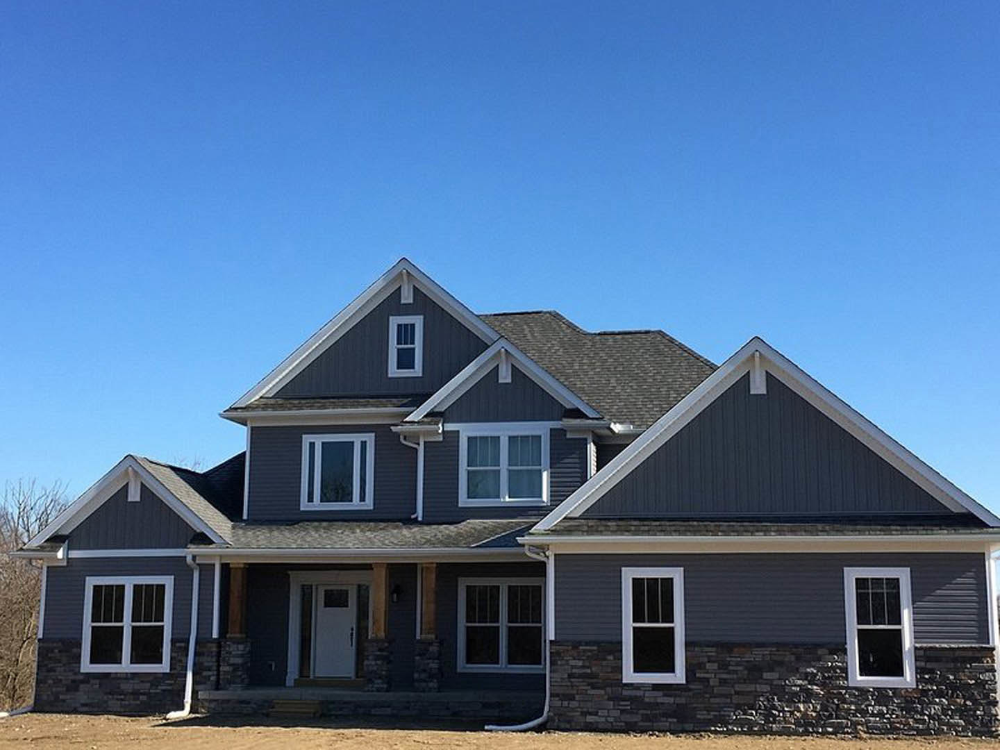 White siding cottage with white-framed windows, white front door featuring a black sign, and covered porch beneath a clear blue sky