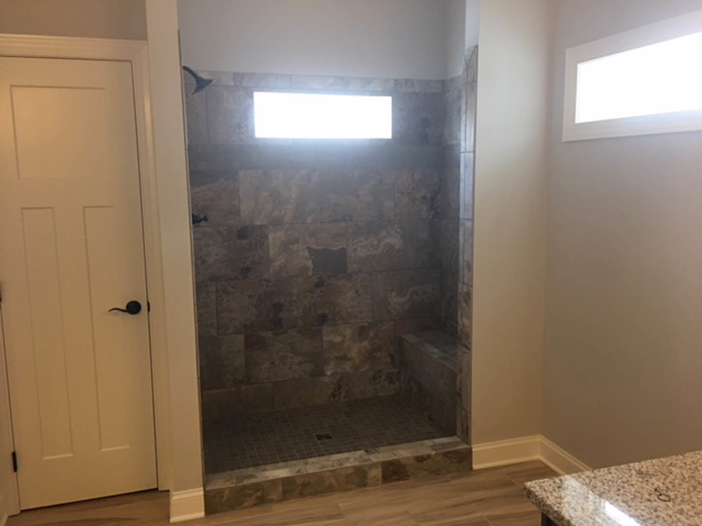 Glass-enclosed shower with white tile walls, built-in niche, window for natural light, and black hardware adjacent to a white door in a modern bathroom.