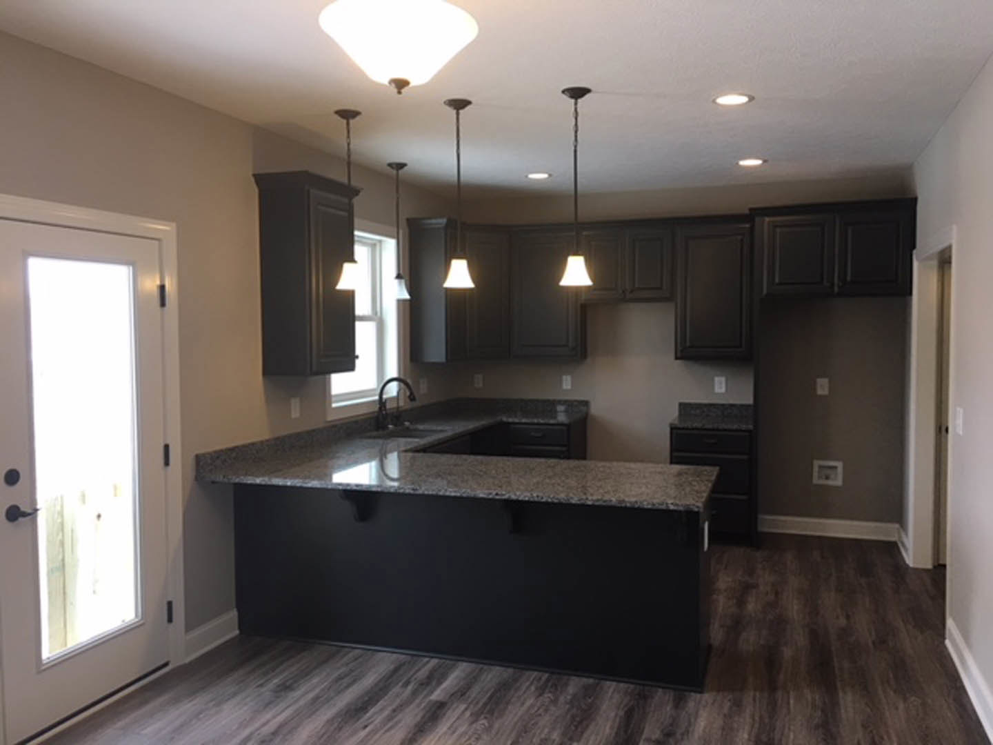 Marble countertop kitchen with wood flooring, white cabinetry, stainless steel sink, and recessed lighting