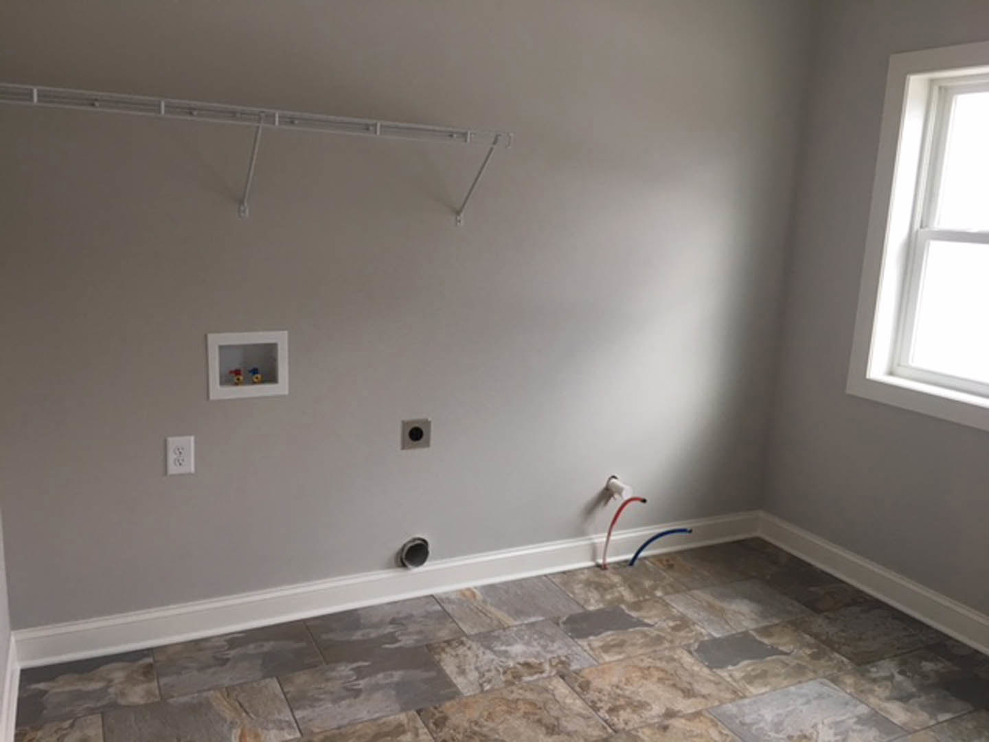 Sunlit room featuring light ceramic tile flooring, plaster walls, a large window with white trim, and a white electrical outlet.