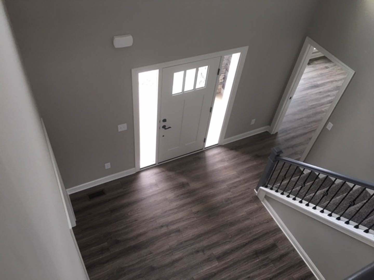 Hallway with dark wood laminate flooring, white doors, staircase with white handrail, open door leading to a room, white rectangular object on gray surface, plaster walls and
