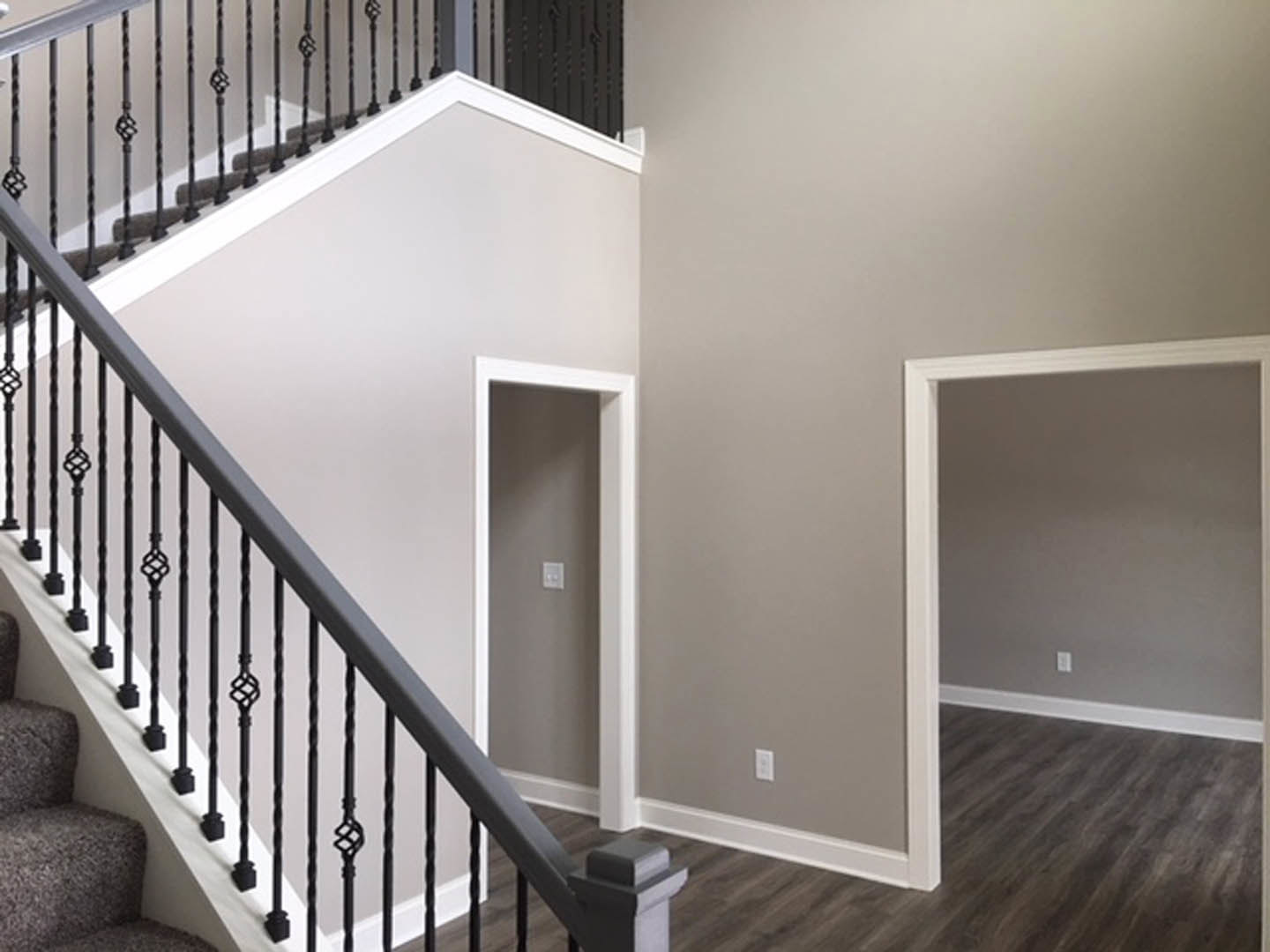 Modern staircase with black metal railings, light wood steps, white walls, hallway with light switch, and doorway leading to adjacent room