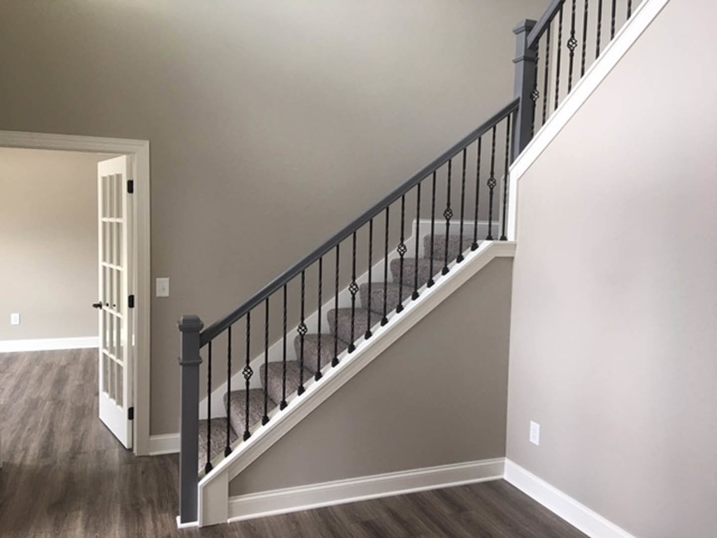 White staircase with black metal railing, light wood flooring, and white plaster walls adjacent to a closed white door