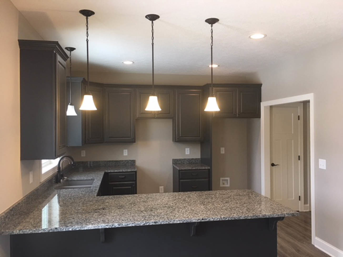 Granite countertop and matching island in a modern kitchen with white cabinetry, stainless steel sink, black hardware, and a white door
