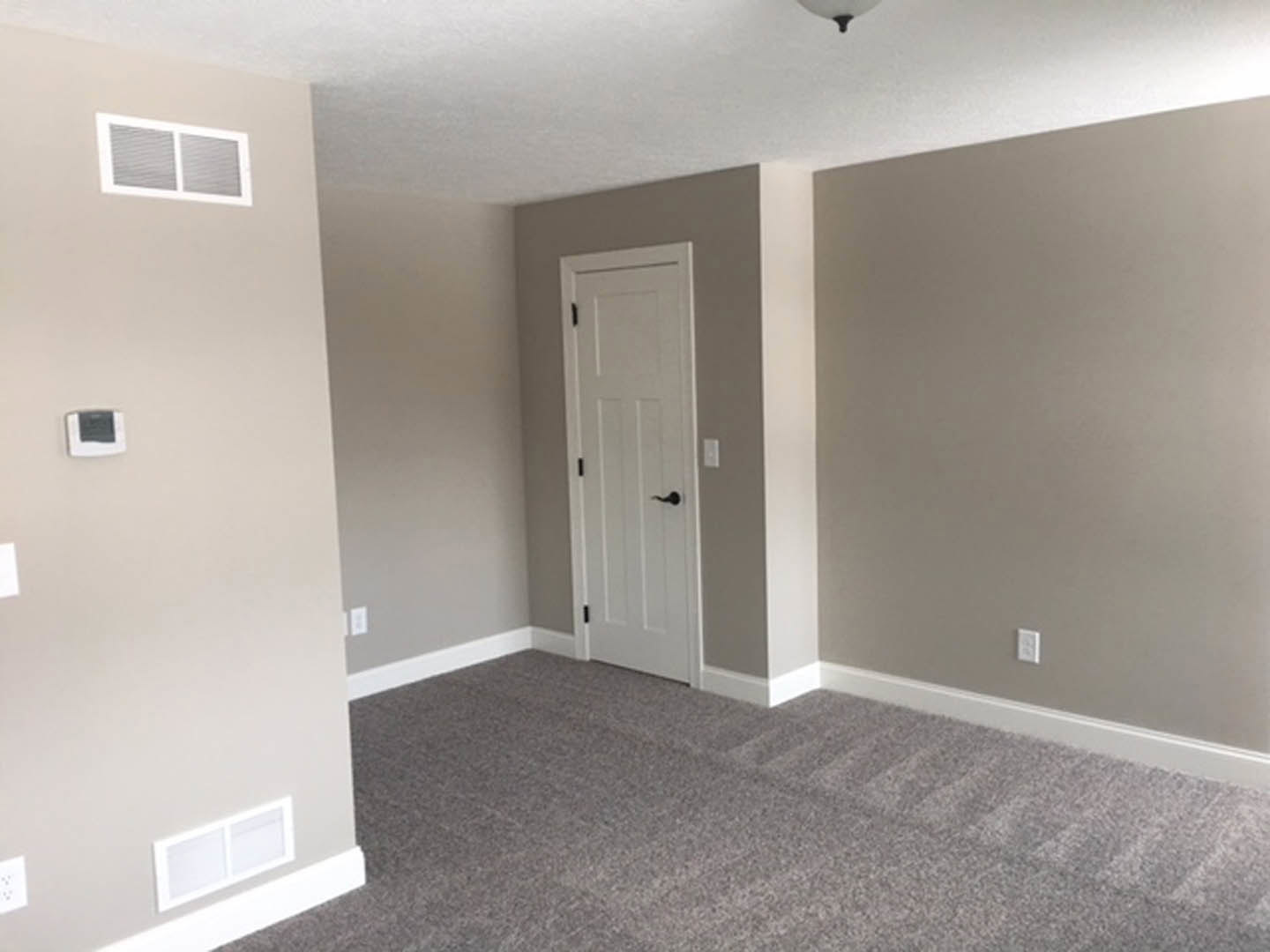 White paneled door with black lever handle, beige carpet flooring, white walls with baseboard molding, ceiling vent visible