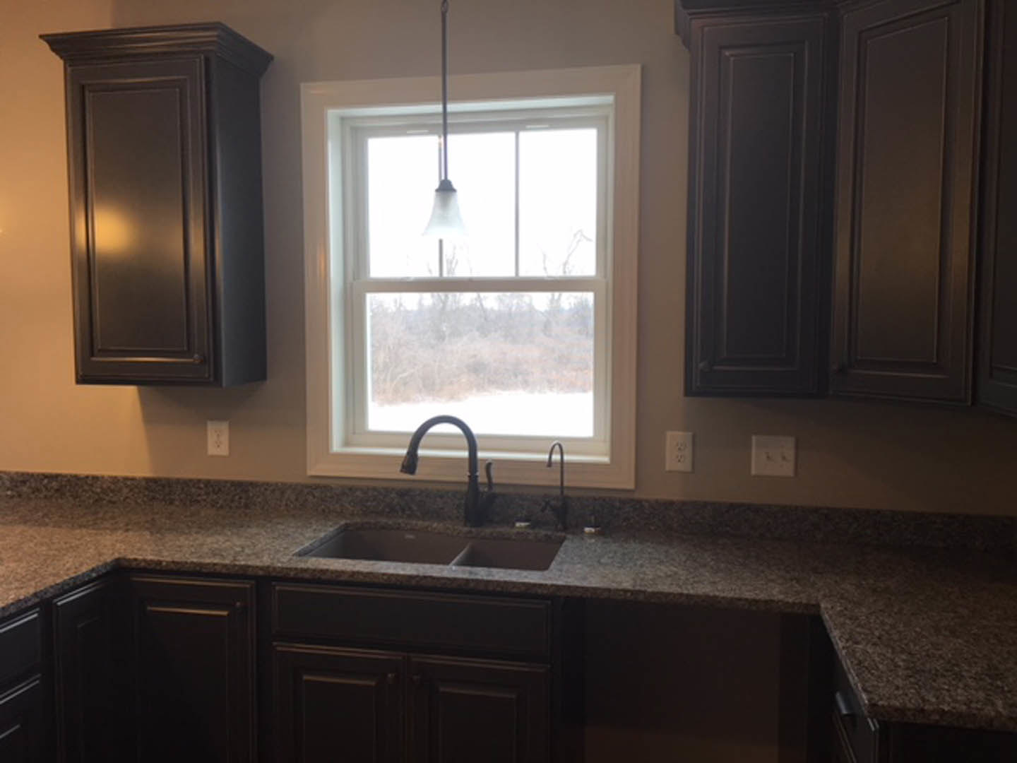 Modern kitchen featuring white shaker cabinets, stainless steel sink with chrome faucet, light stone countertop, and sunlight streaming through nearby window.