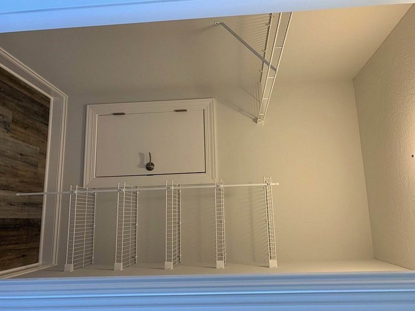 White built-in shelves and cabinet with metal handle beside a white ladder mounted on the wall, blue and white striped surface visible, door leading to adjacent room, plaster walls